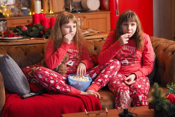 Kırmızı pijamalı iki genç kız film izliyor ve patlamış mısır yiyorlar..