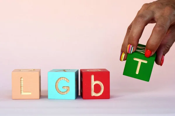 A woman\'s hand with rainbow nails lays out the inscription LGBT from cubes. abbreviation LGBT on a pink background. High quality photo