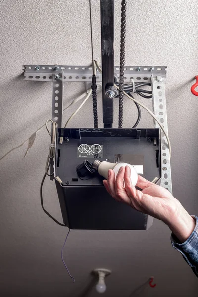 Man replaces a light bulb in a garage door opener with an LED