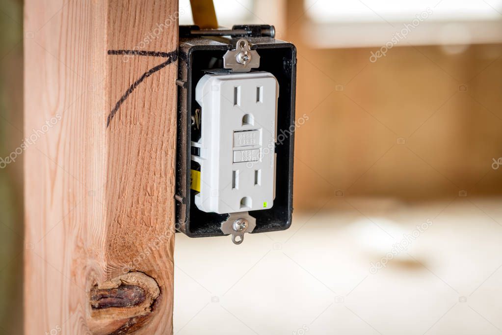 White plastic electrical outlet mounted in a box and a wood stud