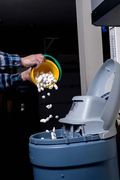 Az ember megsavanyít sót egy vízlágyító egy sárga vödör — Stock Fotó