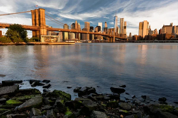 Brooklyn Bridge and rocky shore with the New York skyline — Stock Photo, Image