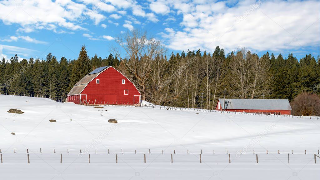 Bright red barn in winter with clouds fence and snow