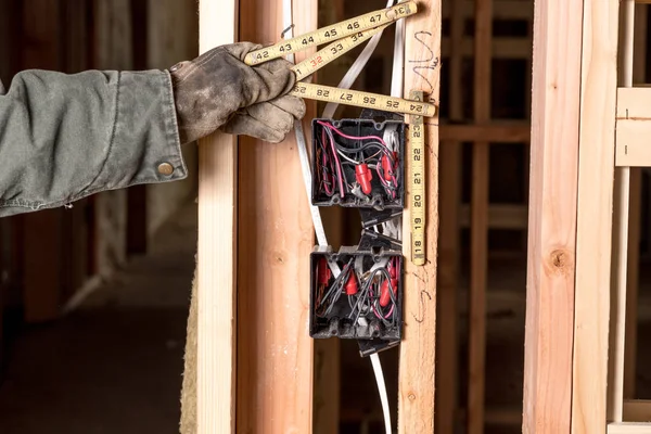 House builder uses an old wooden ruler to measure electrical box