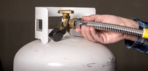 A handyman tries to hook up a stainless-steel line to a propane 