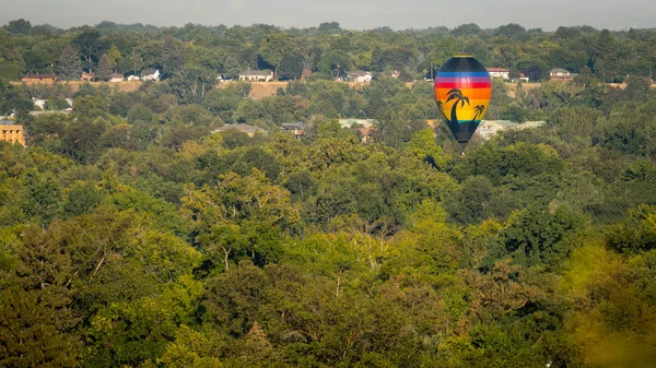Une seule montgolfière flotte au-dessus de la ville des arbres au-dessus d'un blan — Photo