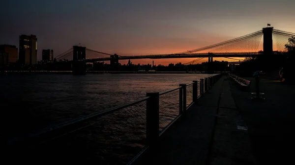 Silhuett av Brooklyn Bridge vid soluppgången med reflektion i — Stockfoto