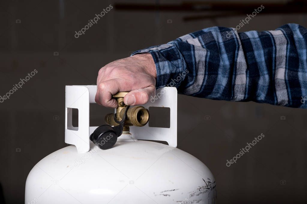 Man tightens the knob on a white propane tank with his hand