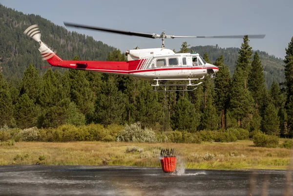 Fire fighter in a helicopter getting water from a lake — Stock Photo, Image