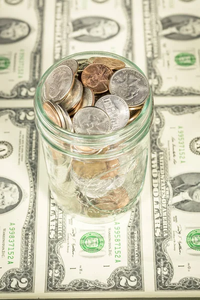 Glass jar filled with coins witting on bills — Stock Photo, Image