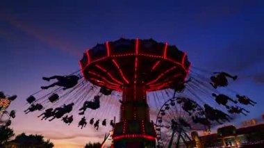 Gecenin gün batımı saatinde etrafında dönen salıncaklarla fuarda eğlenceli bir yolculuk