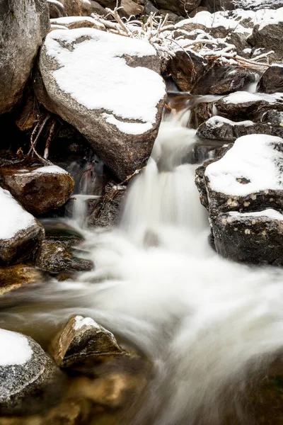 Snow covered rocks align a small waterfall — Stock fotografie