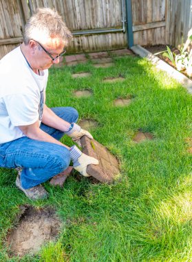 Bahçe düzenleyicisi çimlerle kaplı bir avludan bir kaldırıcı tuğla kaldırıyor.