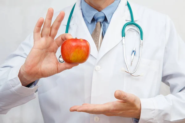 Doctor shows a red apple as a concept for a healthy diet and lifestyle or a good diet.