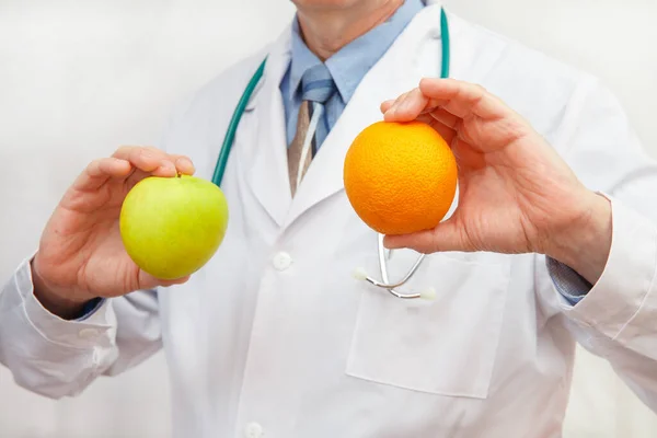 医者は健康的な食事やライフスタイルや良い食事のための概念としてリンゴとオレンジを保持しています — ストック写真