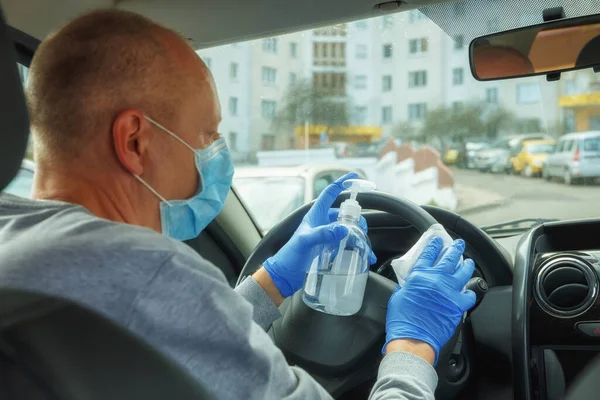 Car disinfection. A man in gloves and a mask wipes the steering wheel with a disinfectant wipe.