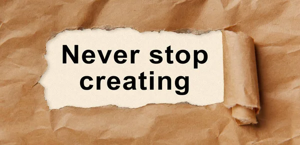 Text Never Stop Creating Appearing Torn Brown Paper — Stock Photo, Image