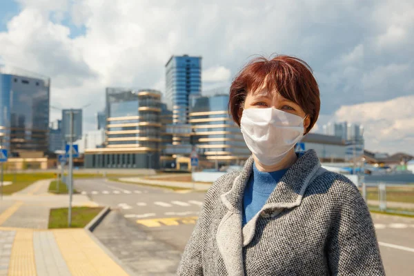 Woman on a city street in an empty city in a mask for the protection of Coronavirus Covid-19. Portrait of a woman on the background of business buildings.
