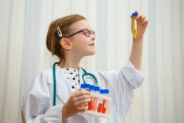 Little girl in a doctor s smock examines test tubes with tests. Educational medical game.