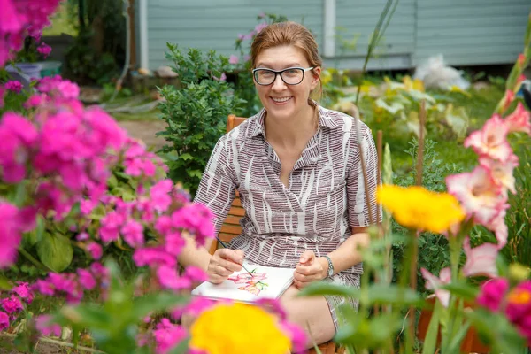 A woman sits in a garden among flowers and draws from nature.