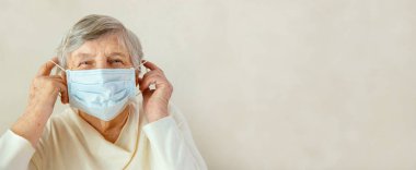 Yaşlı bir kadın yüzüne tıbbi maske takıyor. Tıbbi maskeli kadın koronavirüs için endişeleniyor.
