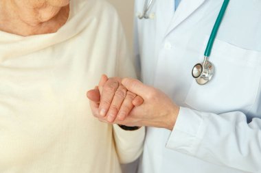 Yardım eden eller, yaşlı bakım konsepti. Doktorun eli bir kadının elini tutar.