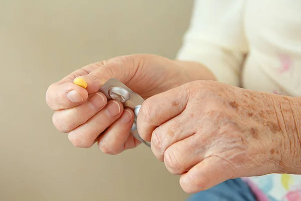 An elderly woman is going to swallow a medicine, a pill and drink it with water. Closeup of a hand with a tablet.