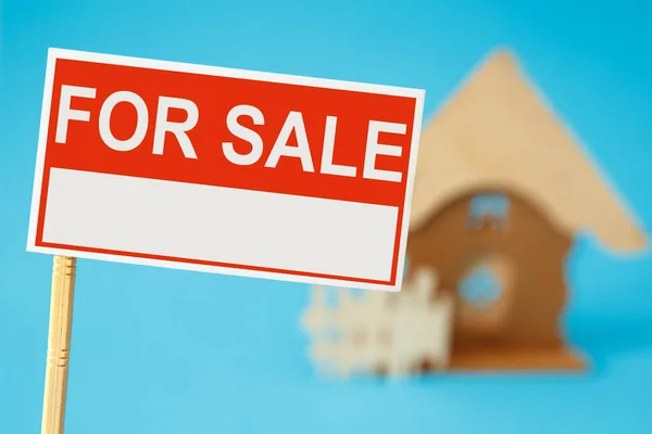 A sign for the sale of real estate and a house in the background. Real estate sale concept