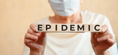 Yaşlı bir kadın elinde EPIDEMIC yazısıyla tahta küpleri tutuyor. Tıbbi konsept