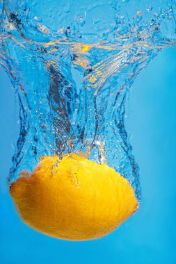 Suda taze limon damlaları ve mavi bir arka plan.