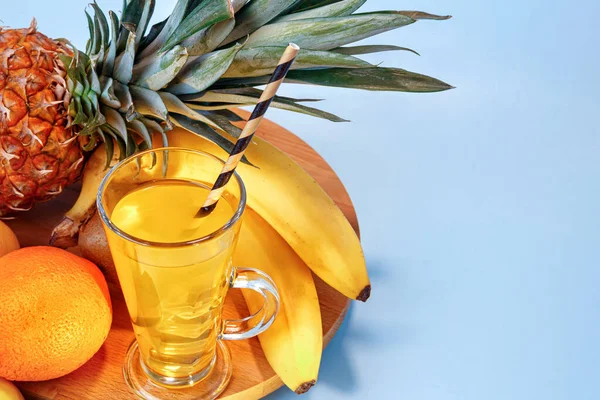 Fresh multifruit juice with ice in a glass. Pineapple, orange, banana, lemon, apple on a blue background