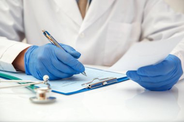 Koruyucu eldivenli bir doktor ilaç için reçete yazar..