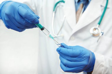 Koruyucu eldivenli doktor tıbbî bir şırıngaya ilaç çekiyor.