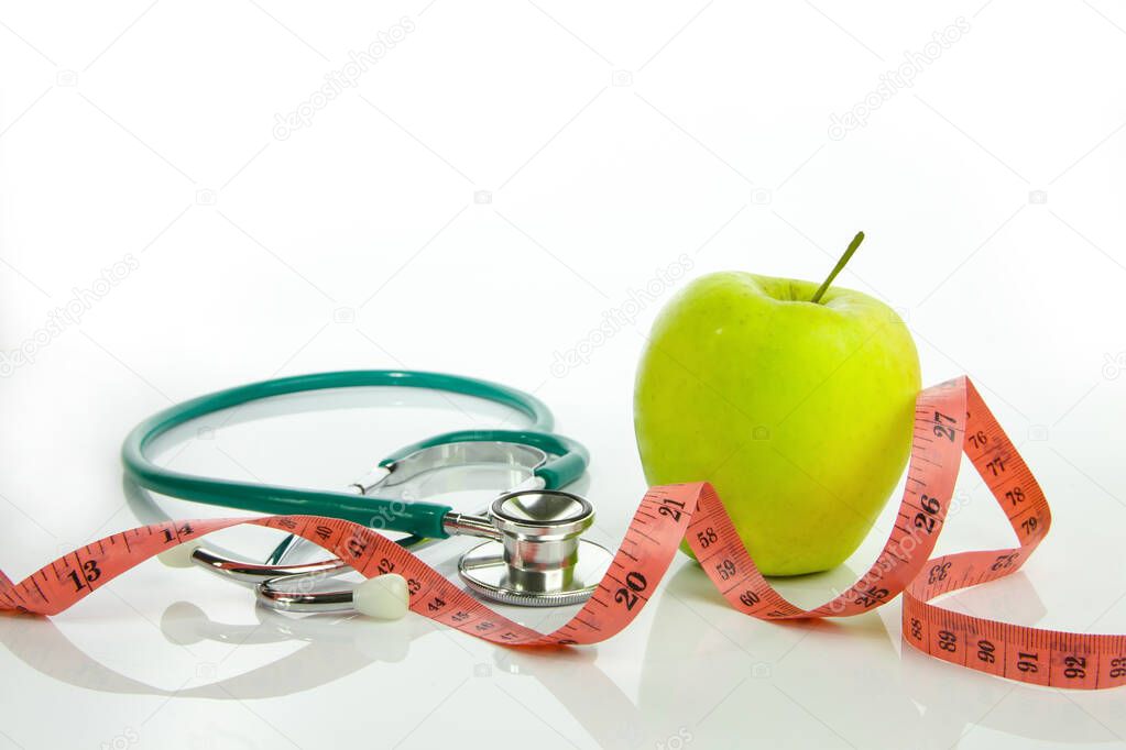 Green apple with tape measure and stethoscope on a white background. Diet and weight loss concept