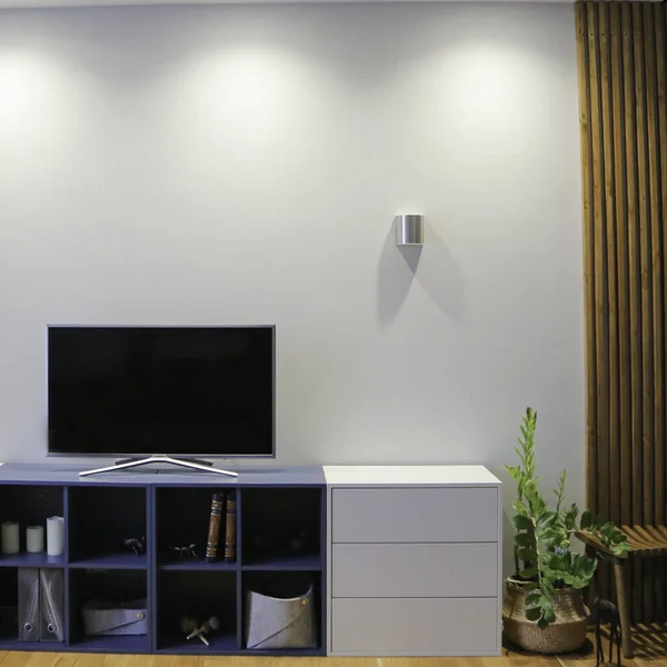 TV on a sideboard in the living room with a wooden floor and gray walls and slats in a minimalist style