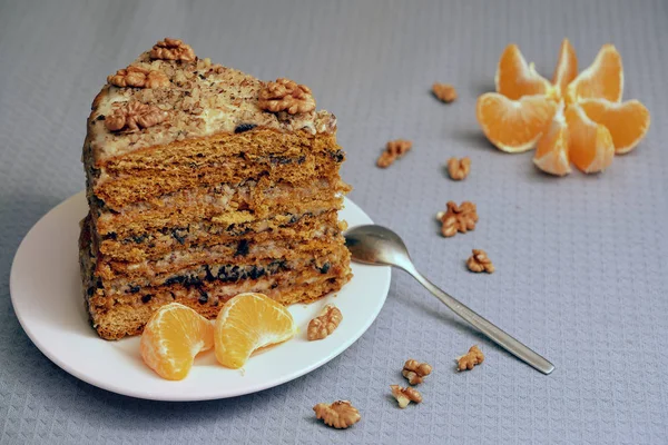 A large piece of homemade honey cake on a porcelain plate with nuts and mandarin