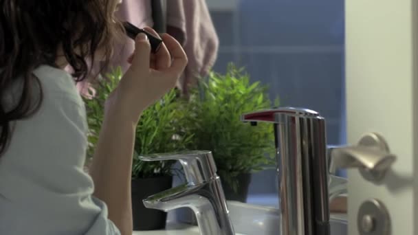 Красива молода жінка використовує помаду, дивлячись у дзеркало у ванній кімнаті, камеру на повзунку — стокове відео