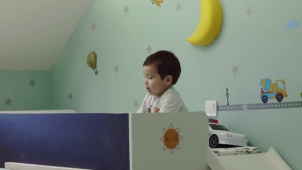 Criança brincando com brinquedos coloridos na cama branca em seu quarto, câmera no controle deslizante — Vídeo de Stock