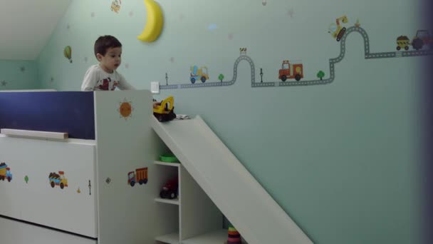 Słodkie dziecko siedzi na jego łóżko w pokoju dla dzieci i zabawki koparka gry i szczęśliwy twarz wesoły, aparat na suwak — Wideo stockowe