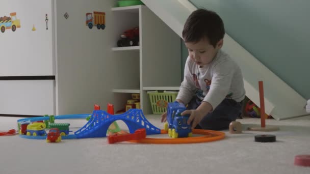 Dziecko gry ciężarówka pociąg zabawki na dywanie w pokoju dzieci i uśmiech do kamery z tła childs łóżko, aparat na suwak — Wideo stockowe