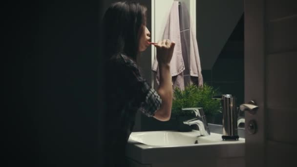 Mujer joven cepillándose los dientes en el baño por la noche, cámara en el control deslizante — Vídeo de stock