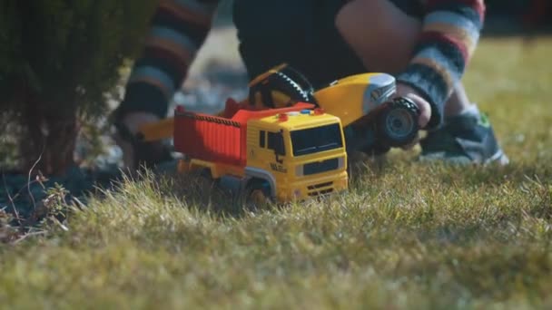 Uma criança brinca no jardim com carros de brinquedo, uma escavadeira, um caminhão, câmera no controle deslizante — Vídeo de Stock