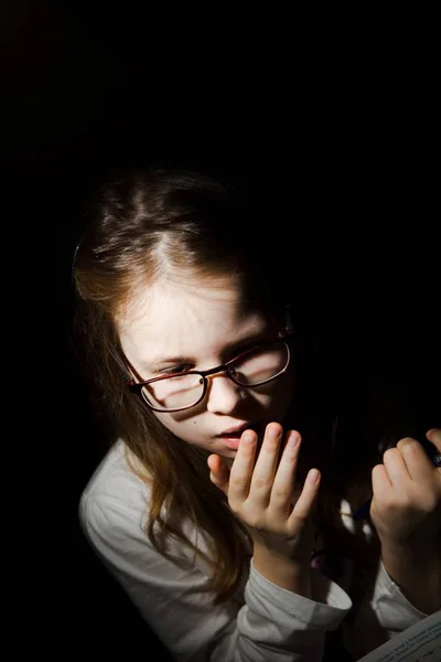 Young girl feared while reading book. Black background. Fear worries and scare. Naturally processed photo.