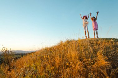 Neşeli çocuklar atladı ve ellerini kaldırdı. Gün batımından sonra yaz günü sırasında yakalanan duygu.