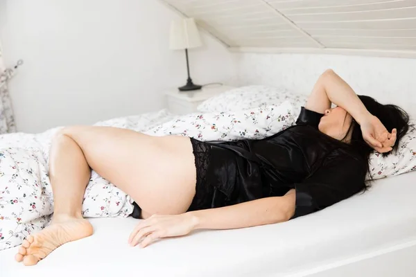 Ung attraktiv kvinna sova halv naken i sängen i svart morgonrock. — Stockfoto