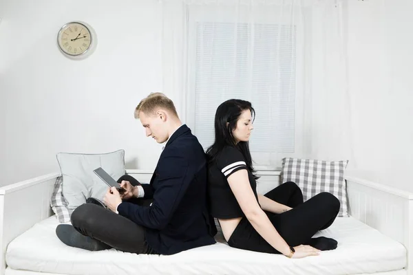 Mann arbeitet am Tablet und sitzt auf dem Bett zurück zu seiner Freundin — Stockfoto