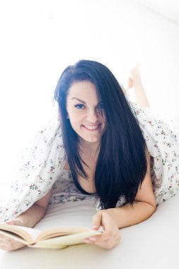 Genç kadın rahatlatıcı ve okuma kitap içinde yatak odası