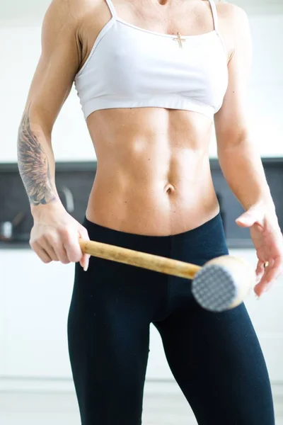 Fitness woman with workout body in kitchen posing with meat mallet.