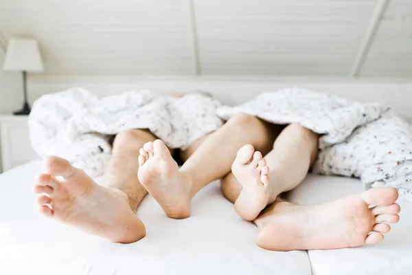 Beine von Mann und Frau auf weißem Bettlaken, teilweise mit Bettdecke bedeckt - Vorderansicht. — Stockfoto