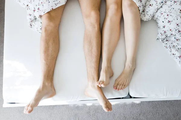 Beine von Mann und Frau auf weißem Bettlaken, teilweise mit Bettdecke bedeckt - Ansicht von oben — Stockfoto